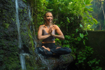 outdoors adventure portrait of young beautiful and happy woman doing yoga and meditation exercise sitting in lotus posture on rock at tropical rainforest enjoying nature