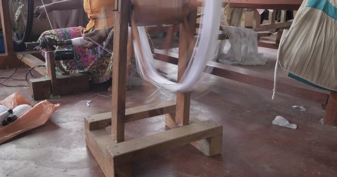 Hands of an old woman using an old spinning wheel to turn wool into yarn
