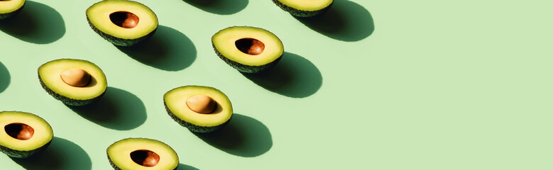 Avocado cut in half in sunlight. Neo mint green background. Front view.