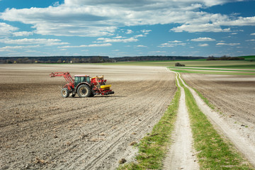 Agricultural tractor in a plowed field, long dirt road and clouds on a blue sky