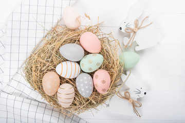 Easter table setting, holiday table home decor idea, flat lay composition with white plates, cutlery, colorful pastel painted Easter eggs, festive decor and fresh spring flowers