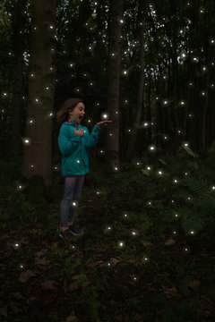 Full Length Of Girl Standing Amidst Fireflies At Night In Forest