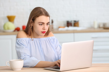 Beautiful young woman with laptop in kitchen