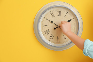 Little boy touching arrows of clock on color wall