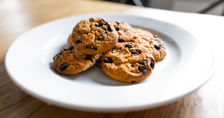 Basic drop cookies with chocolate morsels. Choc chip cookies in a white plate on a wooden table. Close-up of homemade chocolate chip cookies. Traditional handmade chewy cookies with chocolate chunk