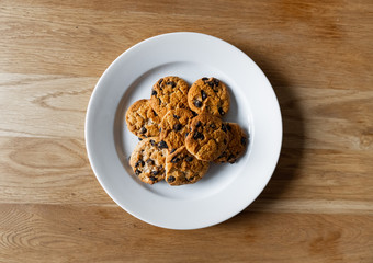 Top view of homemade chocolate chip cookies. Choc chip cookies in a white plate on a wooden table. Basic drop cookies with chocolate morsels. Traditional handmade chewy cookies with chocolate chunk