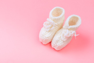 knitted baby booties on pastel pink background.