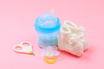 safe scissors, soother, orthopedic feeding bottle  and booties for babies on pastel pink background .