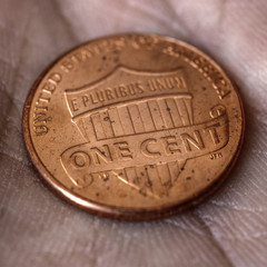 American US coin 1 cent penny lies on a dirty palm close up. An impressive, dramatic square shot with an aged effect. Low-wage labor work, poverty, homeless people. Macro