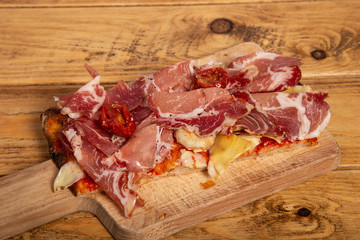 slice of homemade rectangular pizza with onion, raw parma and dehydrated tomatoes on wooden cutting board.