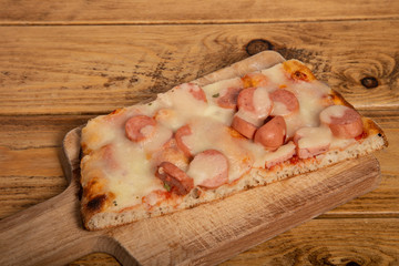Slice of homemade pizza with frankfurt on a wooden cutting board.
