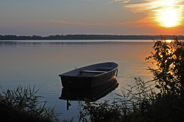 Naklejka na ściany i meble Ein Boot liegt auf einem See zum Sonnenaufgang