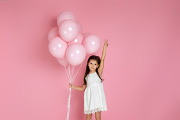 Smiling adorable little child girl with pastel pink air balloons showing victory gesture isolated over pink background. Beautiful happy kid on a birthday party. space for text