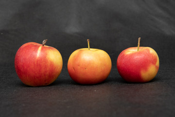 Three ripe fresh organic sweet red apples with yellow spots, closeup, on black background
