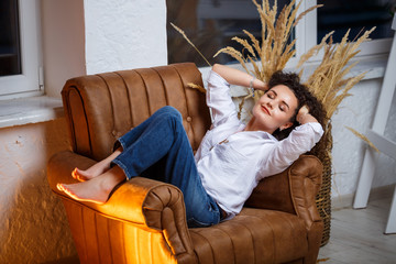 Obraz premium Beautiful young girl model with curls posing. She is wearing a white shirt and jeans.