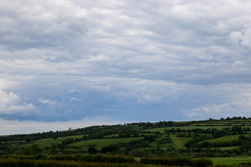 Fototapeta na wymiar View over the fertile rural agricultural landscape of County Meath, Ireland in summer with its patchwork of rich green fields divided by the lush tree lined hedgerows and blue cloudy sky above