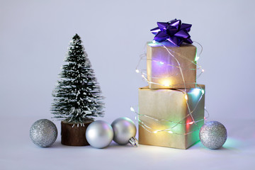 Gifts in craft paper boxes wrapped in blinking lighting garland and Christmas tree and balls on the grey  background. Happy Christmas
