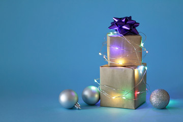 Gifts in craft paper boxes wrapped in blinking lighting garland and Christmas balls on the blue background. Happy Christmas
