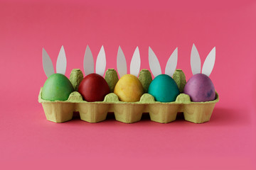 Easter eggs painted in colorful paints with funny rabbit ears are vary on pink background. Happy Easter day! Holiday card
