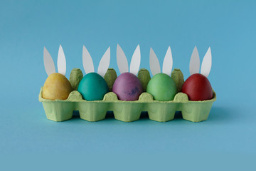 Easter eggs painted in colorful paints with funny rabbit ears are vary on blue background. Happy Easter day! Holiday card, handmade
