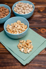 Assorted nuts in dishes on wooden table. Pistachios, cashews, almonds