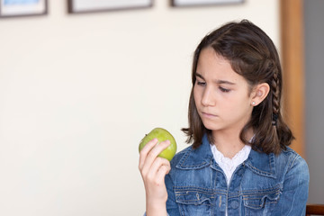 little girl looking unhappy at a green apple
