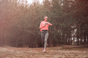 Woman running in the woods and checking smartwatch. Young girl jogging in a forest. Healthy...