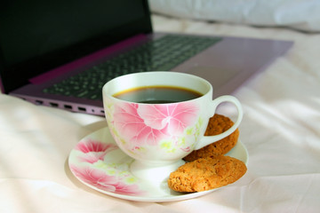 A cup of tea with cookies on a pink bed with a purple laptop. Remote work at home.