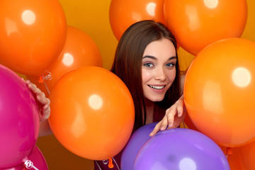 Fototapeta na wymiar Smiling caucasian girl posing with bright color air balloons on yellow background. Beautiful happy young woman on a birthday holiday. close-up
