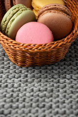 Top view of colored macarons in small basket, with selective focus, on gray knitted blanket, vertically, with copy space