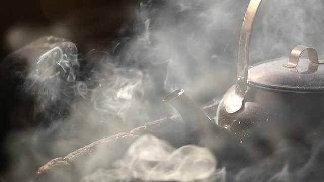 Steaming Hot Kettle on Firewood Outdoors Starts to Boil. Close Up