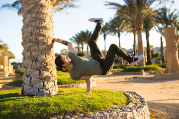 Athletic young handsome man,doing a handstand on summer holiday,relaxing in beach hotel resort with palm trees,b-boy breakdancing outdoors,workout