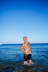 Fototapeta na wymiar Happy man guy joy on vacation, stands at sea and splashes in the water. Men's shorts, sun, beach