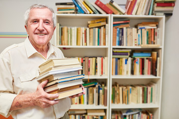 Zufriedener Senior als Bibliothekar mit einem Bücher Stapel in einer Bibliothek