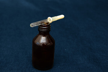 a glass dropper with a yellow rubber tip lies on a dark brown bottle on a blue trend background closeup