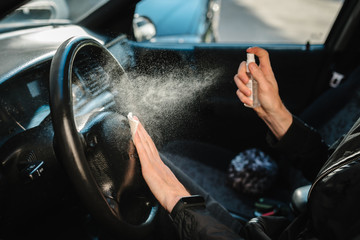 Spraying antibacterial sanitizer spray on steering wheel car, infection control concept. Prevent...