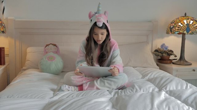 joven con larga melena y pijama mono de unicornio sentada en cama habla por skype en tableta