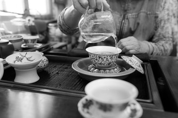 Gong Fu Cha brewing using a porcelain gaiwan and a glass justice/fairness cup. Traditional chinese tea drinking method. Black and white photography