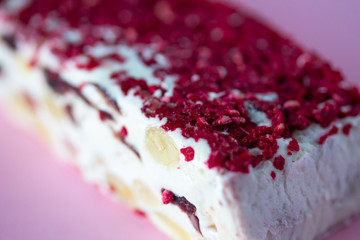 Torrone or nougat bar with nuts and red dried berries. Traditional italian dessert close up on pink background. Sweet tasty and healthy food