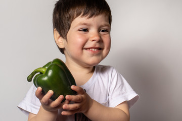 Fototapeta premium Little boy holds green pepper in his hands. Proper nutrition of children. Green vegetables in the diet of children.