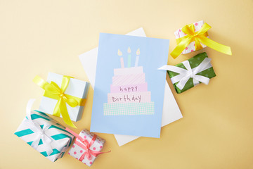 top view of festive colorful gifts and happy birthday greeting card on beige background
