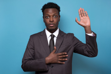 African american male in suit raising palm and holding hand on chest