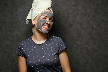 Beautiful young girl with a tonic foam mask on her face and a towel tied with hair