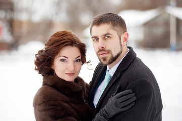 Girl with makeup and hairstyle hugs a bearded man in a coat in a winter park. Winter wedding.