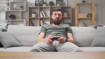 A man is bored at home on the sofa and plays video games - Powered by Adobe