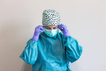 Photo of a nurse dressed in coronavirus protections, with a personalized surgical cap and gown, putting on a surgical mask.