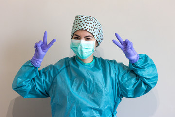 Photo of nurse dressed in coronavirus protections, with a personalized surgical cap, making a peace sign.