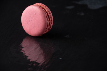 Top view of pink macaron on wet black slate stone, with reflection, horizontal, with copy space