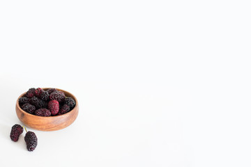 Red and black blackberries in a wooden bowl in the corner on white background.