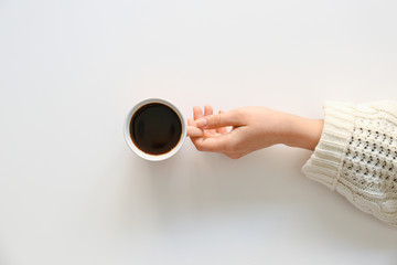 Female hand with cup of hot coffee on light background, top view